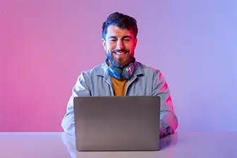 A woman seated at a table, working on a laptop with a camera positioned nearby.