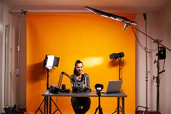 A woman seated at a table, working on a laptop with a camera positioned nearby.